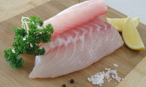 king snapper fillets on wooden board with rock salt, peppercorns and lemon and parsley garnish